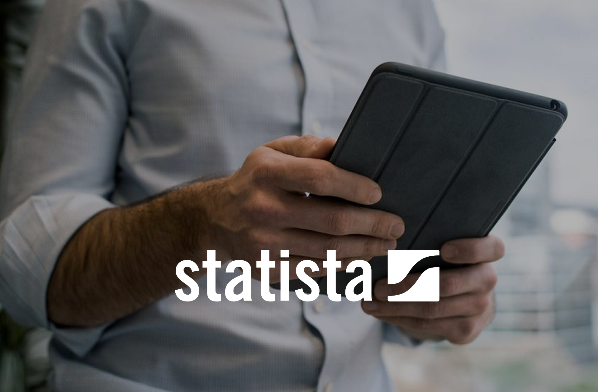 Ein Mann in Hemd hält ein Tablet in der Hand, während das Logo von Statista im Vordergrund sichtbar ist.