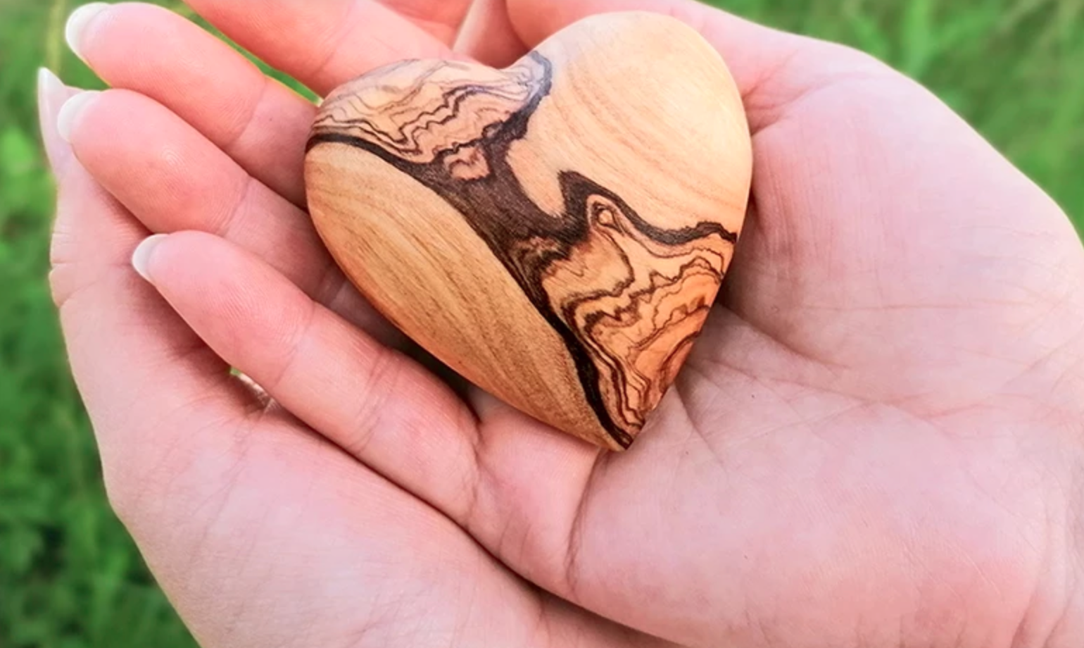 Zwei Hände halten ein Herz aus Holz.